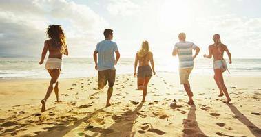 grupo de amigos se divertindo caminhando na praia ao pôr do sol