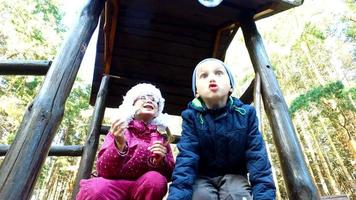 menino e menina loiros com óculos explodem bolhas no playground. as crianças são muito divertidas. eles se divertem e riem.