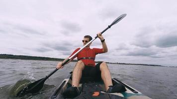 Man kayaking on open water, guy swims in kayak or canoe under dark clouds