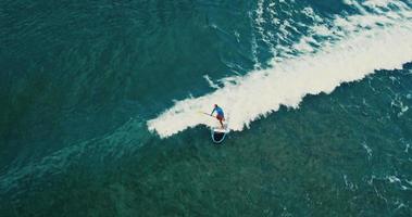 luchtfoto van surfer stand-up paddle boarding op blauwe oceaangolven