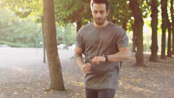 Jeune bel homme à l'aide de smart watch pendant le matin courir dans le parc