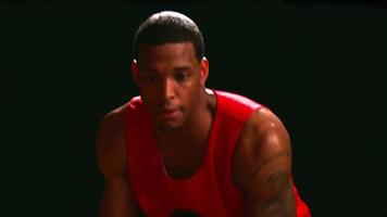 A basketball player dribbles the ball low to the gound against a black backdrop, close up video