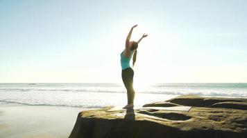 gelukkige jonge vrouw het beoefenen van yoga op het strand bij zonsondergang. gezonde actieve levensstijl concept. video