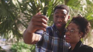 afrikaans amerikaans paar het nemen van de foto van een mobiele telefoon samen voor een palmboom