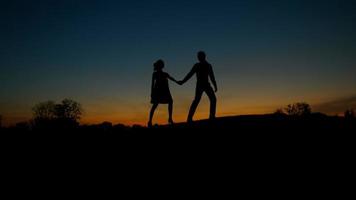 Silhouette of guy and girl walking on the hills. video