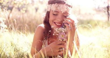 Sonriente niña hippie en un parque sosteniendo flores silvestres