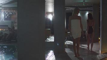 Young attractive woman is walking along the poolside in a towel in a spa wellness center.