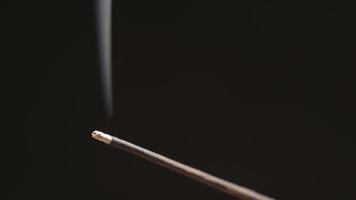 Incense stick smokes on black background close up video
