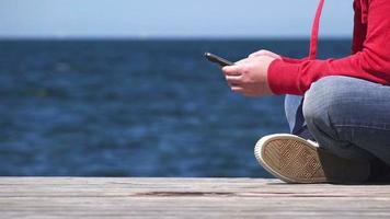 vrouwelijke handen met behulp van mobiele slimme telefoon op oceaanpier