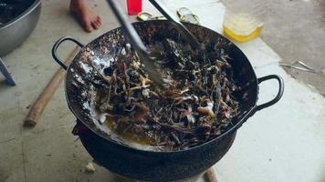 Woman using metal tongs to stir deep-frying frogs in a wok