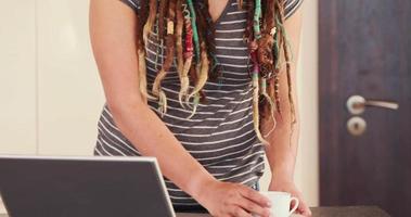 vrouw met dreadlocks met behulp van laptop tijdens het drinken van koffie video