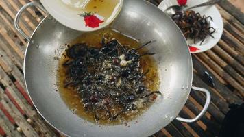 Mujer vertiendo aceite frito en un wok con tarántulas para freír