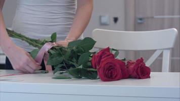 Young woman tying a ribbon bow on red rose bouquet video