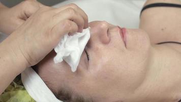 kosmetolog torka ut ögonfransar med våt servett till vuxen kvinna i skönhetssalong