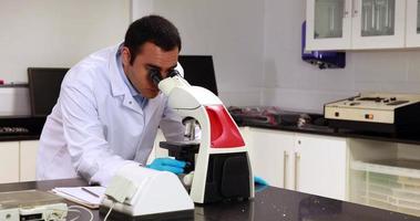 junger Wissenschaftler, der durch Mikroskop im Labor schaut