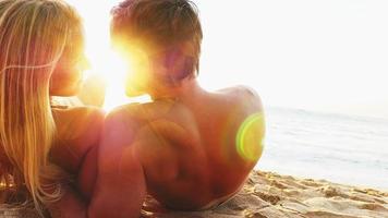 Couple lie on a beach and look out over the ocean at sunset video