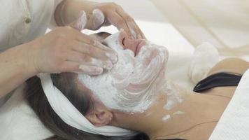 Close up cosmetologist hands rub in mask into girl face, neck in beauty saloon