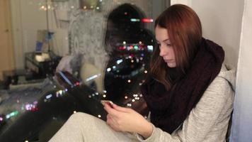 garota sentada no parapeito da janela e usando smartphone video
