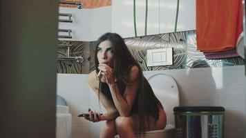 la ragazza si siede sulla toilette con lo smartphone. fumare sigaretta elettronica. rispondere a una chiamata video