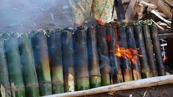 Woman turning bamboo cakes cooking on fire video