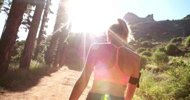 Athletic woman walking away on a mountain nature trail with sunflare