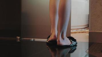 weergave van jonge vrouw in pantoffels lopen naar de deur van de badkamer open en gaan zitten op het bad