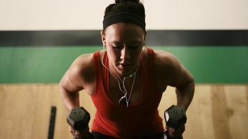 Close up of a fit young woman lifting dumbbells and listening to music in a small gym video