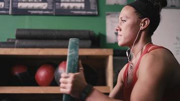 A fit young woman working out with a bumper plate in a small gym while listening to music video