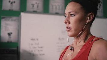 närbild på en fit ung kvinna gör hantel krullar i ett litet gym medan du lyssnar på musik video