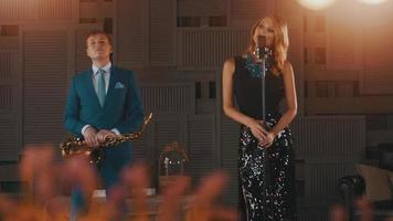Jazzsänger im leuchtenden Kleid am Mikrofon. Saxophonist im blauen Anzug auf der Bühne