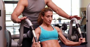 Fit woman using weights machine for arms with her trainer video