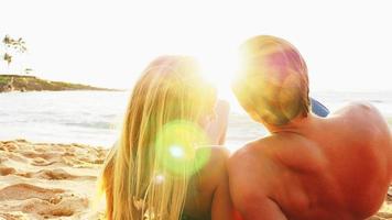 casal deitado em uma praia e olhando para o oceano ao pôr do sol