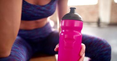 Centrarse en la botella de agua de plástico de colores en el gimnasio durante un descanso de entrenamiento en el gimnasio video