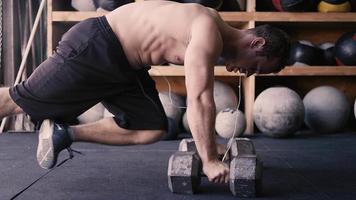 A fit young man doing push-ups with dumbbells in a gym
