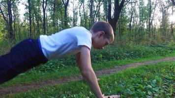 Slim teen boy is wrung out off the ground in the forest. Boy is trained to become stronger. Sports in nature.