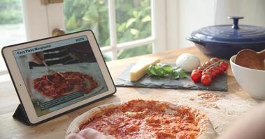 Person, die Pizzarezept mit App auf digitalem Tablet folgt