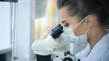 vrouwelijke wetenschapper die door een microscoop in laboratorium kijkt