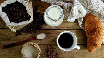 vista dall'alto della mano femminile mettendo zucchero, latte, croissant e tazza di caffè sul tavolo della colazione