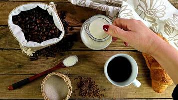 Draufsicht der weiblichen Hand, die Milch in Tasse Kaffee auf Frühstückstisch gießt