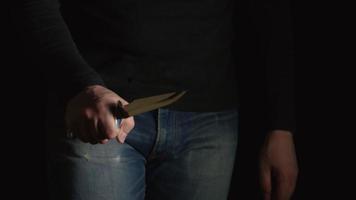 El hombre peligroso con un cuchillo entra en el marco de una oscuridad y sigue adelante. video