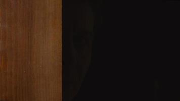menschliches männliches Gesicht schaut von einer Tür aus der Dunkelheit video
