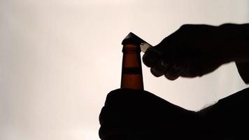 La silhouette des mains mâles ouvrant la bouteille de bière brune avec ouvre video