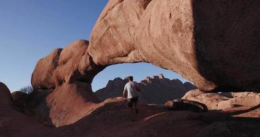 4k mannelijke toerist die de beroemde boog van de spitzkoppe-bergen binnengaat en een foto neemt