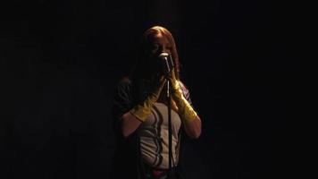 Scrubwoman in gloves sing at vintage microphone on stage under spotlight