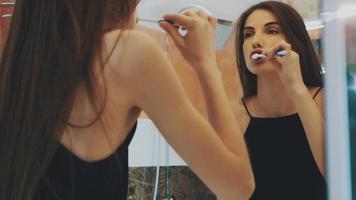 jovem menina morena escova os dentes na frente do espelho no banheiro. reflexão