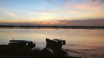 La silueta de la barcaza de dragado por la orilla del río se aleja lentamente de la orilla del río bajo el cielo despejado del amanecer