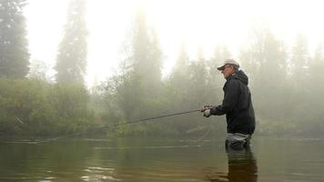 Mann Fliegenfischen in einem Fluss von Nebel umhüllt