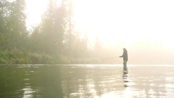 homme pêche à la mouche dans une rivière enveloppée de brouillard