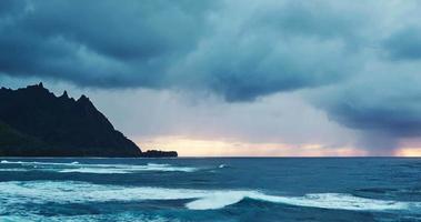 Luftaufnahme, die über Ozeanriff und Wellen in dramatischen Sonnenuntergangssturm am Nordufer von Kauai fliegt