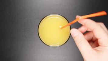 mänsklig hand lägger ett rör till ett glas med en apelsinjuice (ovanifrån)